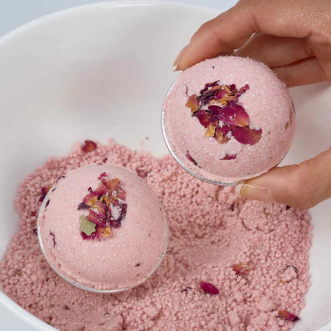 Pink bath bombs with rose petals in a white bowl, held by a hand.