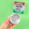 Hand holding a container of putty with packaging labeled 'Super Fun Putty' on a green background