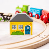 Colorful toy house on a wooden track with toy cars in the background